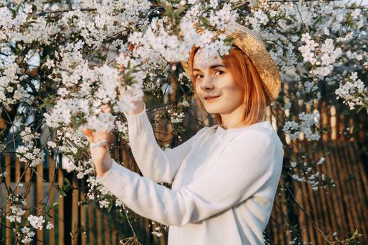 Portrait of a woman in a straw hat in a cherry blossom. Free outdoor recreation, spring blooming garden