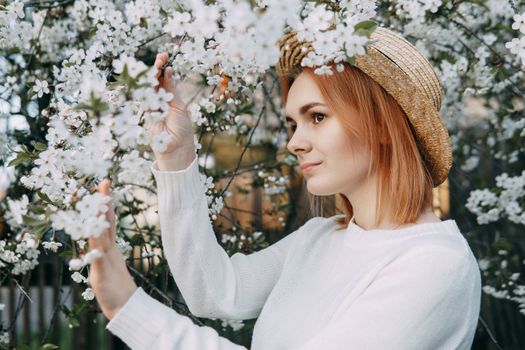 Portrait of a woman in a straw hat in a cherry blossom. Free outdoor recreation, spring blooming garden