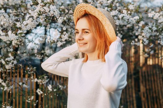 Portrait of a woman in a straw hat in a cherry blossom. Free outdoor recreation, spring blooming garden