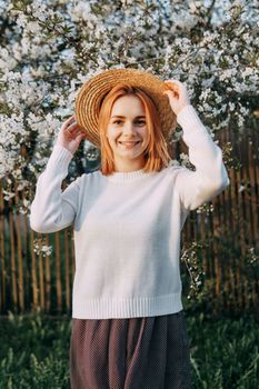Portrait of a woman in a straw hat in a cherry blossom. Free outdoor recreation, spring blooming garden.