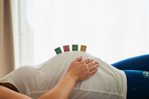 Shes got babies on the brain. an unidentifiable pregnant woman lying on her bed with blocks spelling baby arranged on her belly