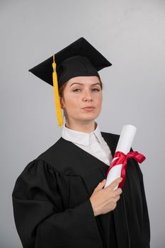 Serious woman in graduation gown holding diploma on white background. Vertical photo