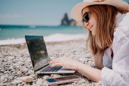 Woman sea laptop. Business woman in yellow hat working on laptop by sea. Close up on hands of pretty lady typing on computer outdoors summer day. Freelance, digital nomad, travel and holidays concept