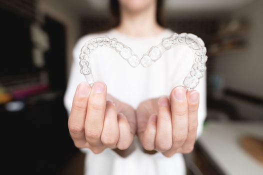 Dental care. Close-up of transparent aligners in the hands of a girl who is standing and showing a heart-shaped orthodontic device to the camera. selective focus.