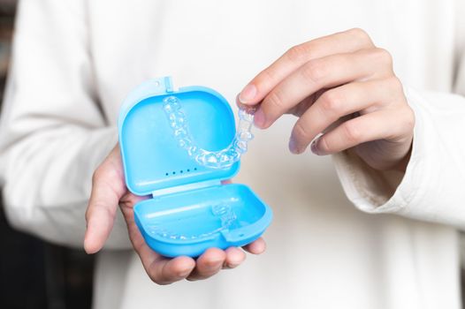 close-up of a young woman with her hand holding a box of dental retainers, invisible. beautiful teeth treatment course concept.