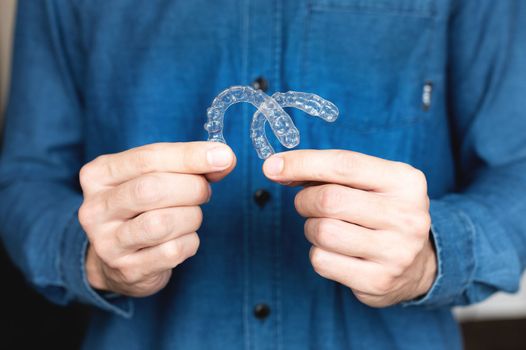 close-up of a young man, holding an invisible tooth alignment retainer in his hands. beautiful teeth orthodontic health concept.