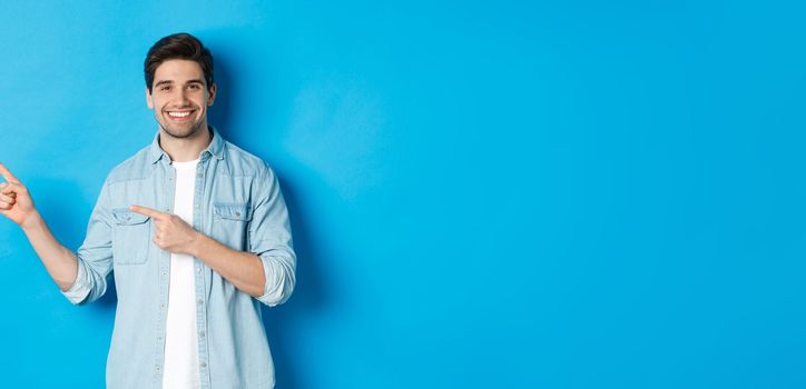 Handsome caucasian man in casual outfit, pointing fingers left and smiling, showing promo offer, standing over blue background.