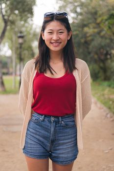 vertical portrait of a smiling young asian woman looking at camera in the park, concept of youth and beauty