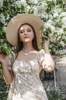 An attractive long-haired woman walks in the spring in the park of blooming apple trees. Spring portrait of a woman