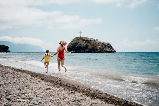 Happy loving family mother and daughter having fun together on the beach. Mum playing with her kid in holiday vacation next to the ocean - Family lifestyle and love concept.