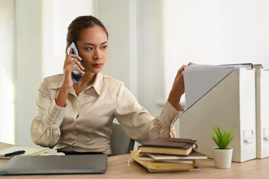 Serious businesswoman having pleasant conversation while sitting at her workstation.