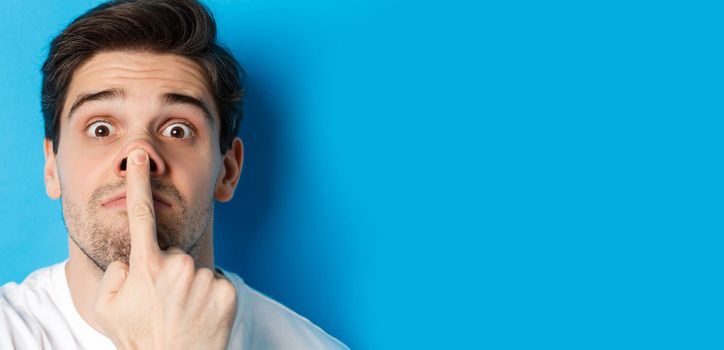 Headshot of caucasian guy making funny expressions, standing over blue background.