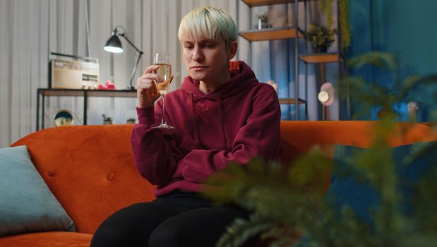 Sad woman girl with short hair sitting at home looks pensive of unrequited love, suffers from unfair situation, drinking champagne. Problem, break up, depressed feeling bad annoyed, burnout bankruptcy
