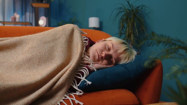 Tired young woman with short blonde hair lying down in bed taking a rest at home room. Carefree girl napping, falling asleep on comfortable sofa with pillows. Closed her eyes enjoy night nap alone