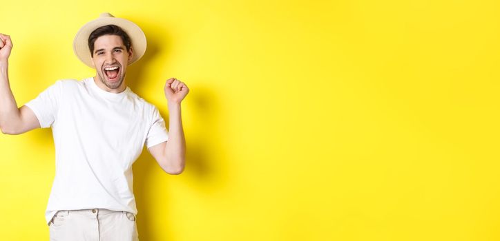 Concept of tourism and lifestyle. Happy man tourist celebrating, rejoicing over vacation, standing over yellow background.