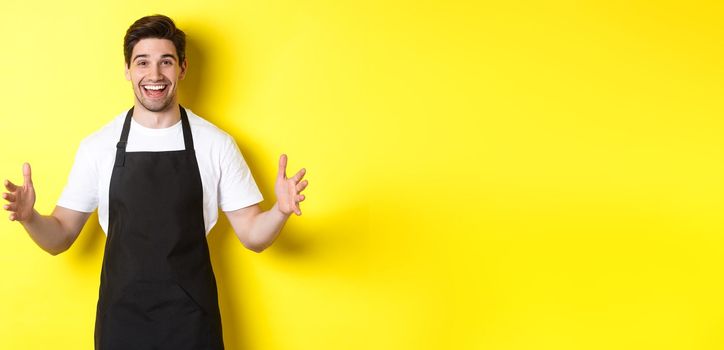 Happy barista holding something big, shaping large object, standing over yellow background.