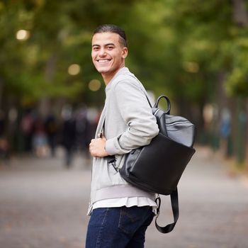 Student portrait and university man travel commute in park with backpack and optimistic smile. Happy, youth and gen z college learner smiling while commuting in New York, USA with bokeh lights.