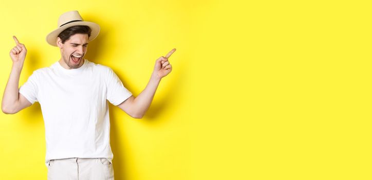 Concept of tourism and lifestyle. Happy man enjoying vacation, tourist dancing over yellow background.