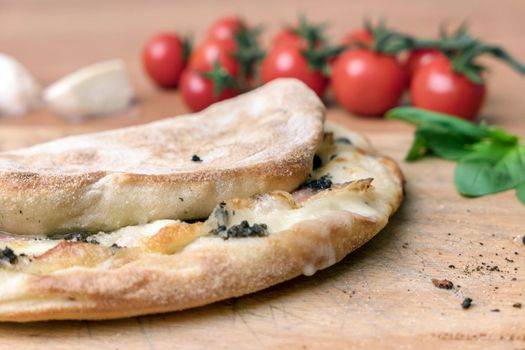 Italian food, closed calzone pizza on rustic wooden background. On blurred background small red tomatoes.
Selective focus