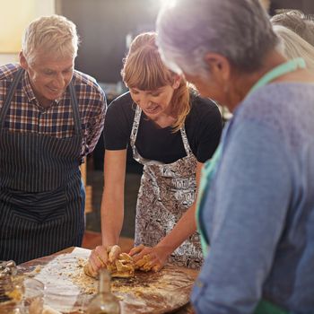 Showing them how to make the perfect dough. a group of seniors attending a cooking class