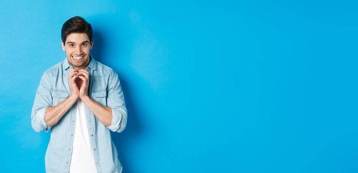 Funny cunning man having evil plan, scheming something and smiling devious, standing against blue background.