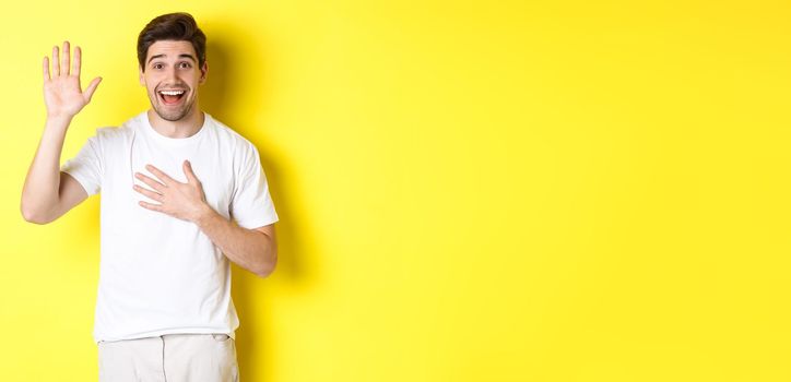 Happy guy making promise, holding hand on heart, swearing to tell truth, standing over yellow background in white t-shirt.