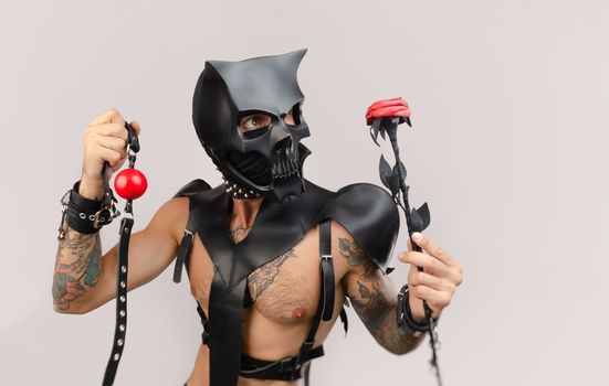 A sexy man in bdsm wearing a demon mask with a whip wearing a leather cloak with leather handcuffs and partuppets on a white background