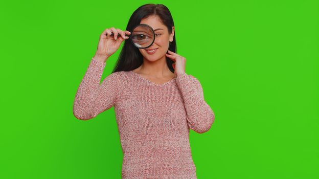 Investigator researcher scientist woman holding magnifying glass near face, looking into camera with big zoomed funny eyes, searching, analysing. Young pretty girl isolated on chroma key background