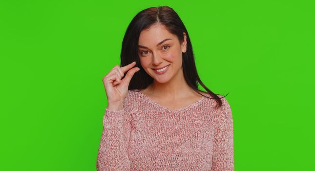 Need some more, please give me. Lovely woman showing a little bit gesture with sceptic smile, showing minimum sign, measuring small size. Young adult girl isolated alone on green chroma key background