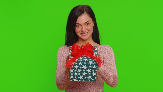 Positive smiling pretty woman presenting birthday gift box stretches out hands, offer wrapped present career bonus, celebrating party. Young adult happy girl isolated on green chroma key background