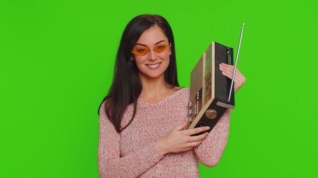 Lovely woman using retro tape record player to listen music, disco dancing of favorite track, having fun, entertaining, fan of vintage technologies. Young adult girl isolated on red wall background