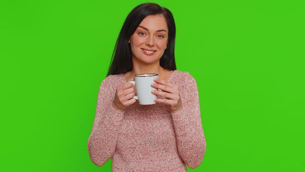 Pretty young woman smelling drinking cup of beverage hot coffee, taking a break, relaxing. Smiling adult girl enjoy to drink aroma tea isolated alone on green screen chroma key studio background