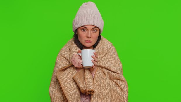 Sick woman wear hat wrapped in plaid shivering from cold, drinking hot tea in unheated apartment without heating due debt. Unhealthy girl feeling discomfort try to warming up on chroma key background