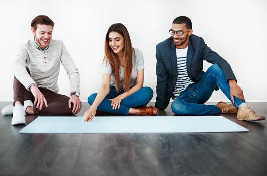 Teamwork from conception to action. Studio shot of a group of young people sitting on the floor and working on blank paper