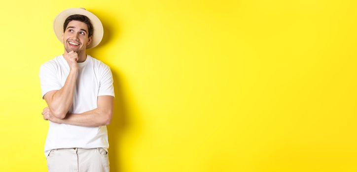 Young thoughtful man tourist imaging something, looking at upper left corner and smiling, thinking and standing over yellow background.