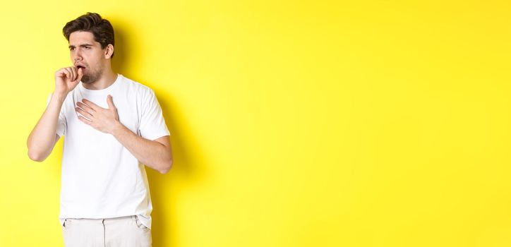 Image of man with covid-19 or flu symptoms, coughing and feeling sick, standing over yellow background. Copy space