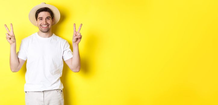 Concept of tourism and vacation. Happy male tourist posing for photo with peace signs, smiling excited, standing against yellow background.