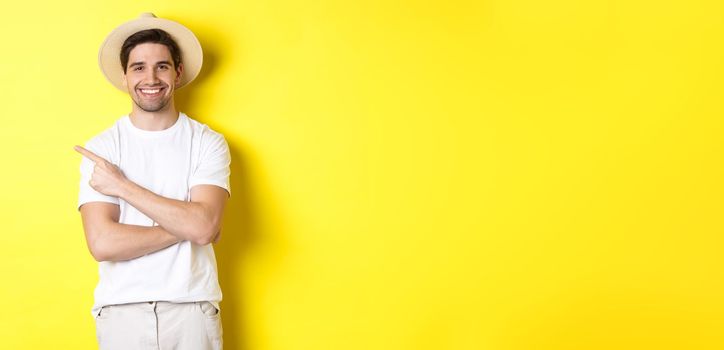 Concept of tourism and lifestyle. Young man tourist pointing finger left, looking happy, showing special holidays promo, yellow background.