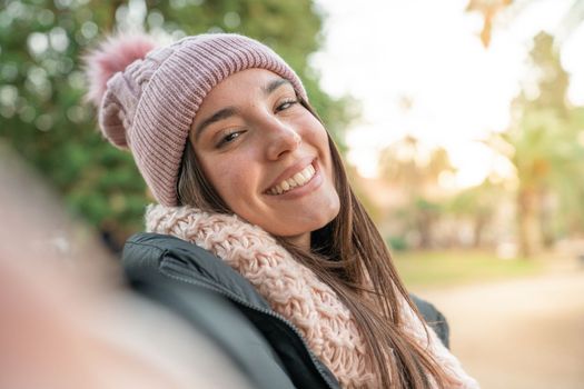 Young beautiful woman smiling taking selfie photo at university campus. Trendy girl with winter hat. Positive cheerful female student posing outdoors for sharing in social media app. Caucasian lady