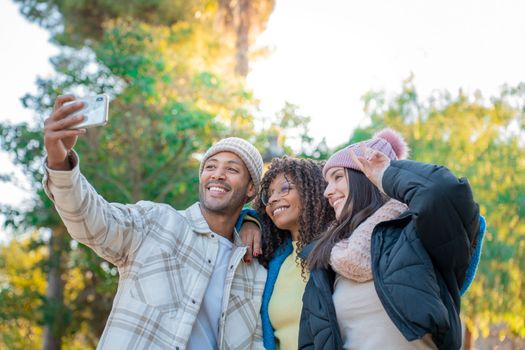 Three cheerful friends taking selfie with phone outdoors. Two girls and one man smiling to take a picture. High quality photo