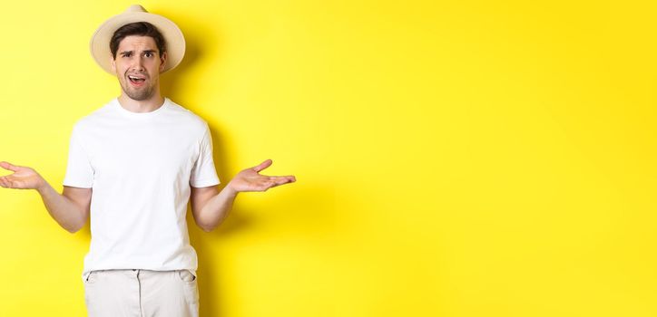 Concept of tourism and summer. Confused guy traveller shrugging, cant understand something, standing against yellow background.