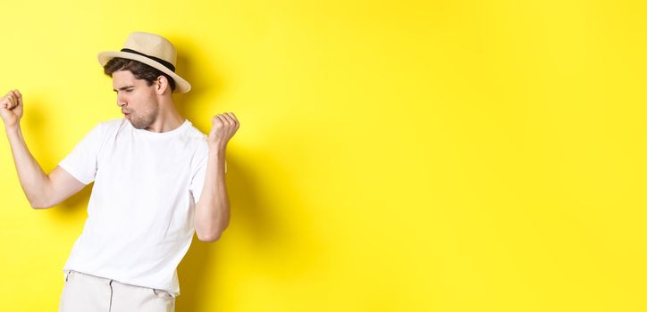 Concept of tourism and vacation. Lucky guy tourist rejoicing, making fist pump and saying yes, standing pleased against yellow background.