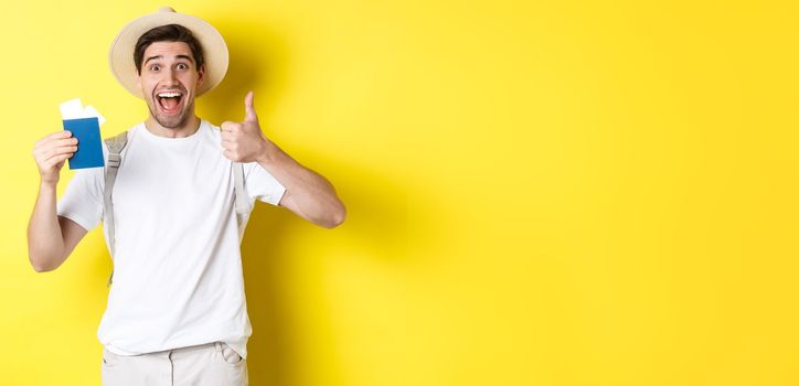 Tourism and vacation. Satisfied male tourist showing passport with tickets and thumb up, recommending travel company, standing over yellow background.