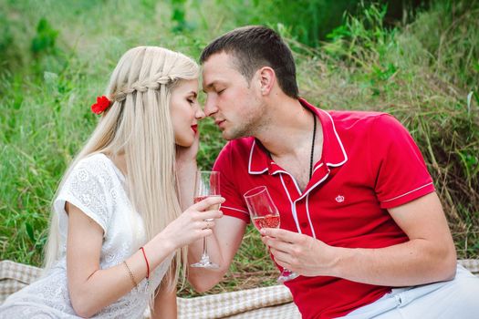 couple in love a blonde girl and a guy in a red t-shirt at a picnic in a park with green grass