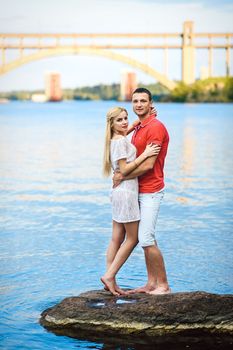 couple in love blonde girl and guy on the river bank at sunset