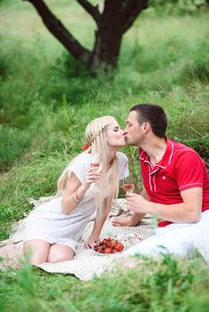 couple in love a blonde girl and a guy in a red t-shirt at a picnic in a park with green grass