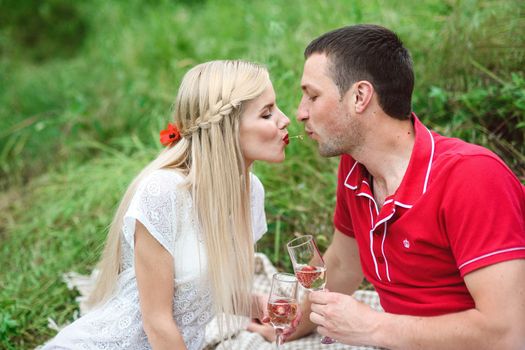 couple in love a blonde girl and a guy in a red t-shirt at a picnic in a park with green grass