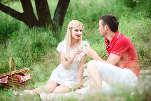 couple in love a blonde girl and a guy in a red t-shirt at a picnic in a park with green grass