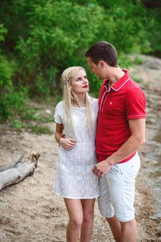 couple in love blonde girl and guy on the river bank at sunset