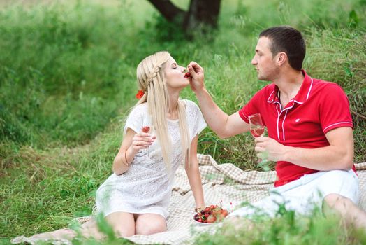 couple in love a blonde girl and a guy in a red t-shirt at a picnic in a park with green grass